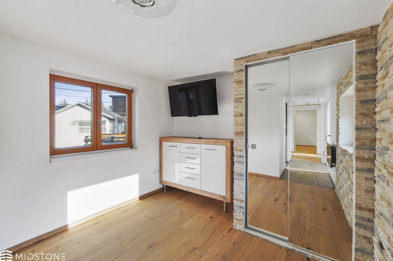 Geräumiges Zimmer mit Holzboden, Steinwandakzent und großem Spiegelschrank.
