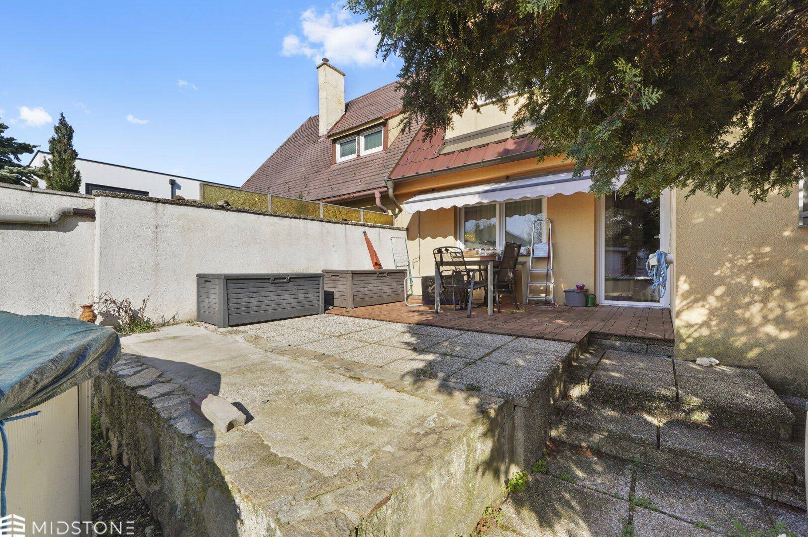 Gepflasterte Terrasse mit Gartenmöbeln, Stauraum und Blick auf das Haus.