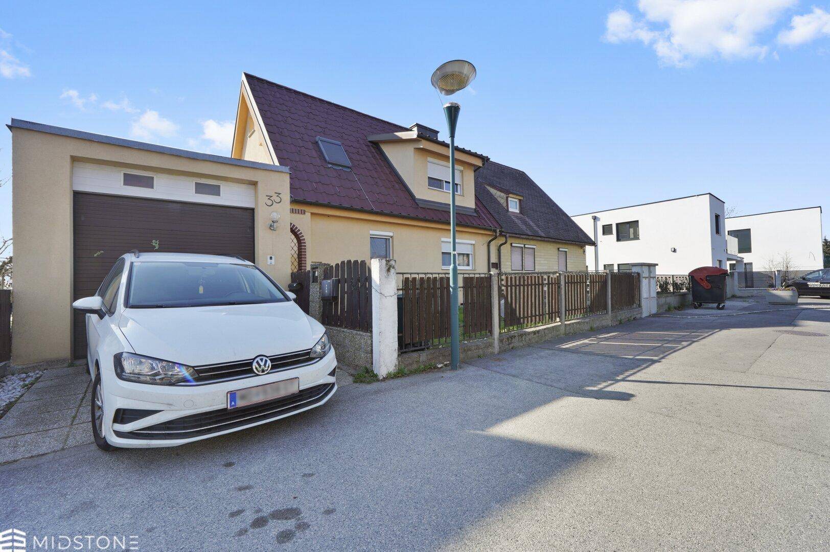 Weitläufige Ansicht des Hauses von der Straße mit Garage und geparktem Auto.