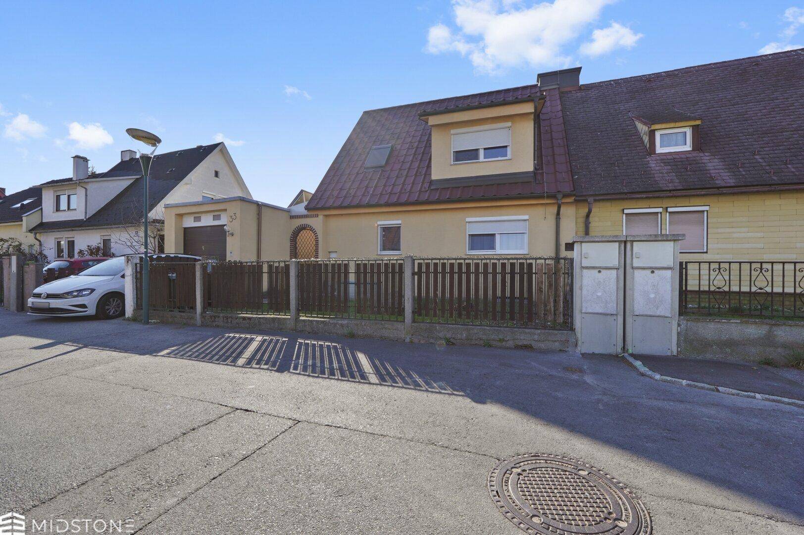 Straßenansicht des Hauses mit Zaun, Briefkästen und angrenzenden Gebäuden.