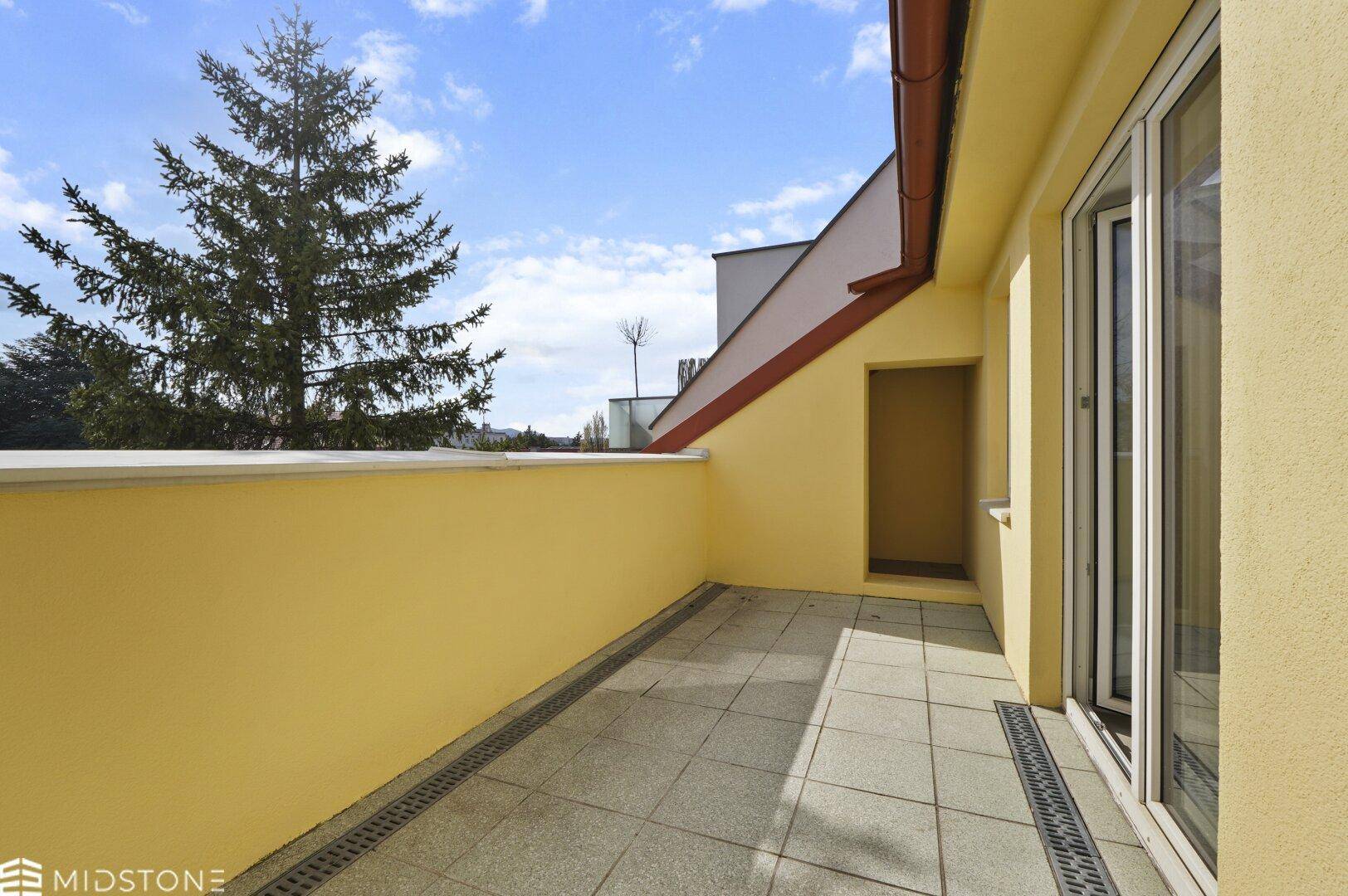 Geräumige Terrasse mit Fliesenboden und Blick auf Bäume und den Himmel.