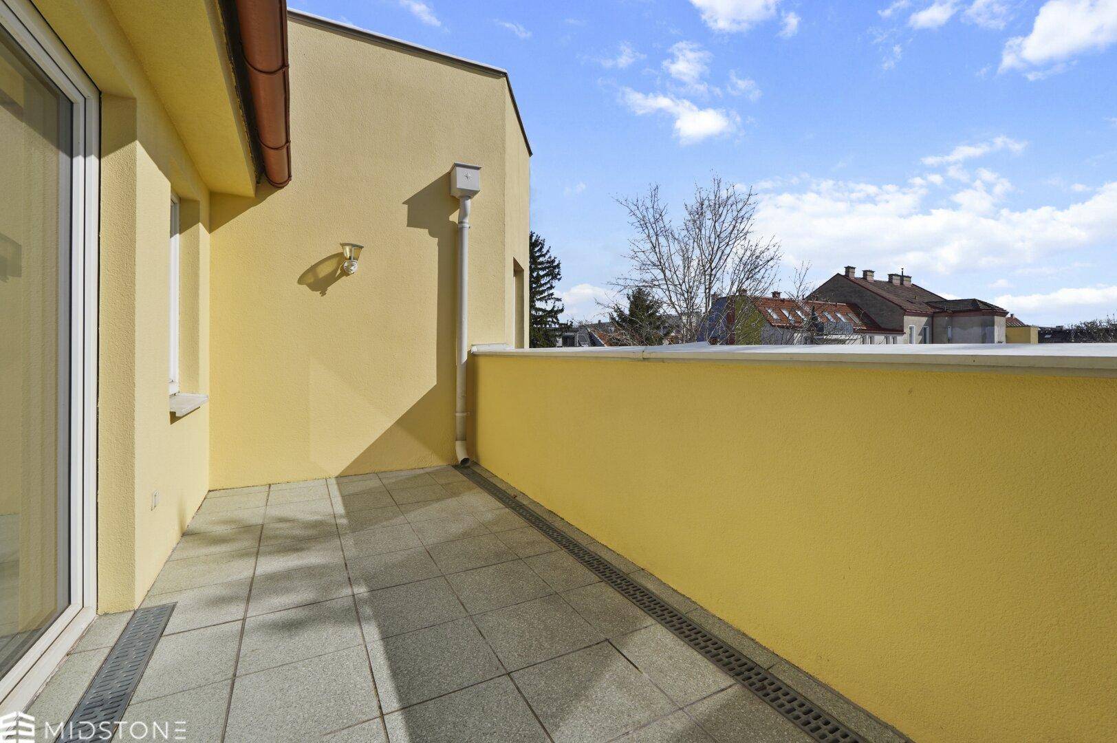 Sonniger Terrassenbereich mit gelber Fassade und weitem Blick über die Dächer.