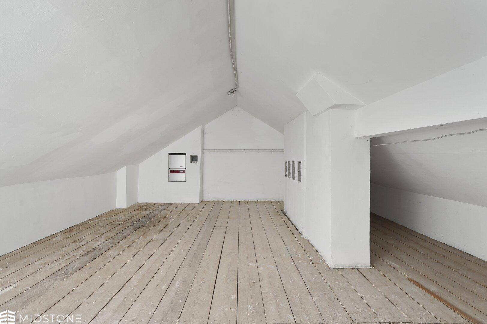 Geräumiger Dachboden mit Holzdielenboden, schrägen Decken und sichtbaren elektrischen Installationen.