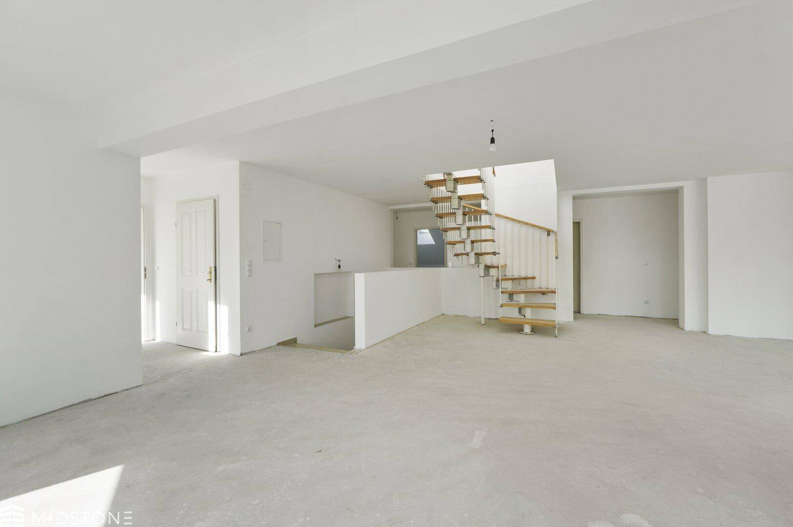 Großer, leerer offener Wohnbereich mit Wendeltreppe und rohem Betonboden, ideal für individuelle Gestaltung.
