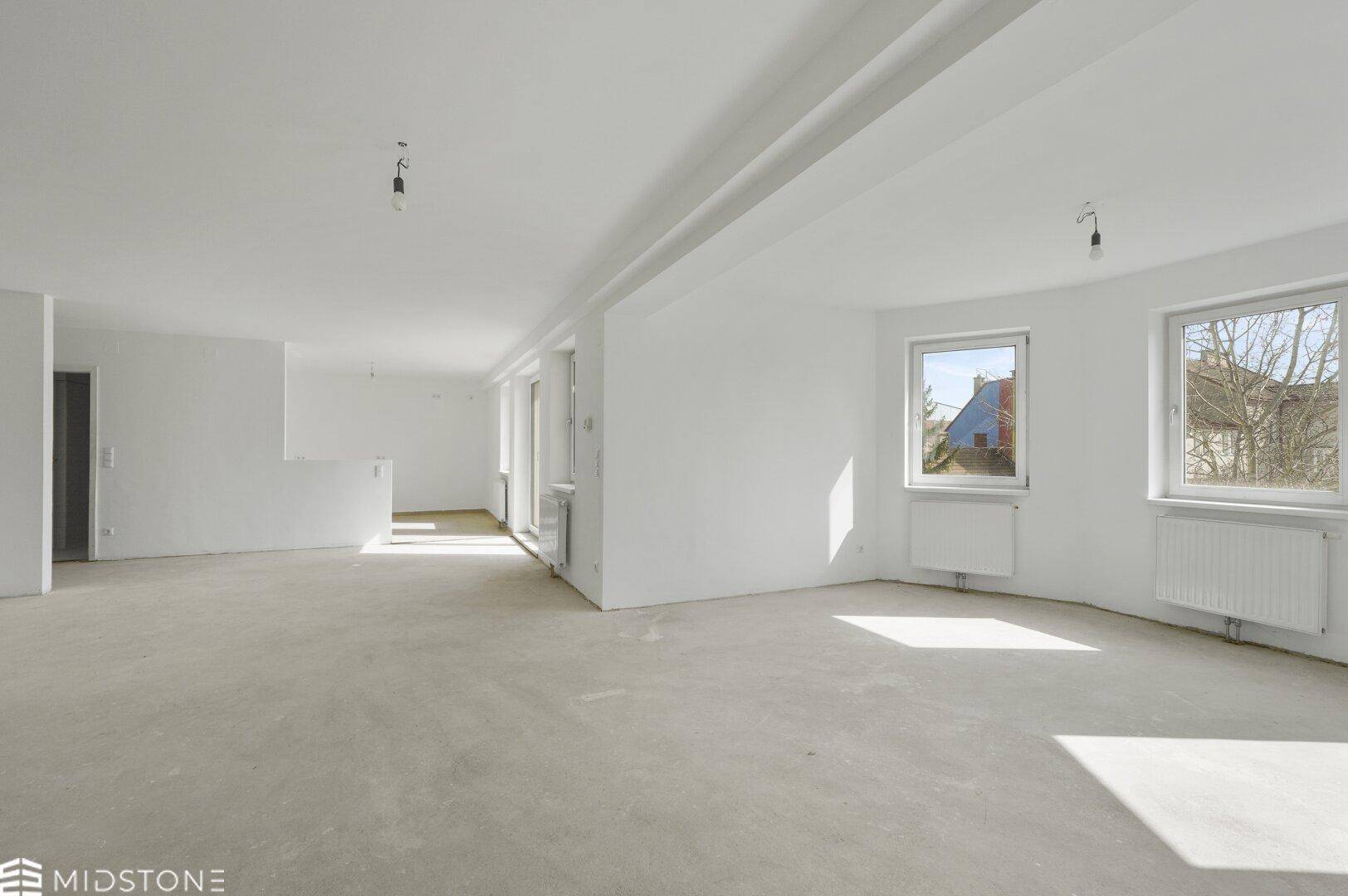 Geräumiger, leerer offener Wohnbereich mit vielen Fenstern und Betonboden, ideal für helle Wohnkonzepte.