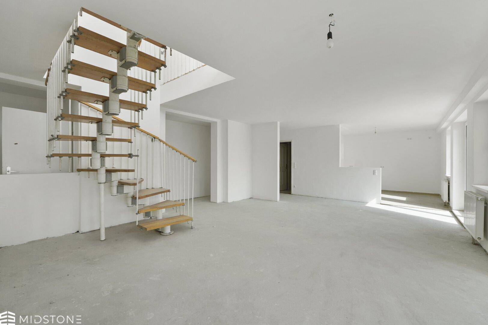 Heller, leerer offener Wohnbereich mit Wendeltreppe und Betonboden, bietet viel Raum für Gestaltung.
