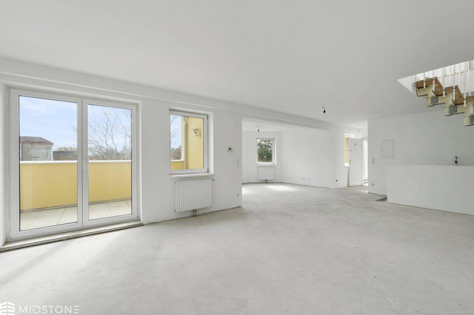 Geräumiger, leerer Wohnbereich mit Zugang zu einem Balkon und Betonboden, lichtdurchflutet.