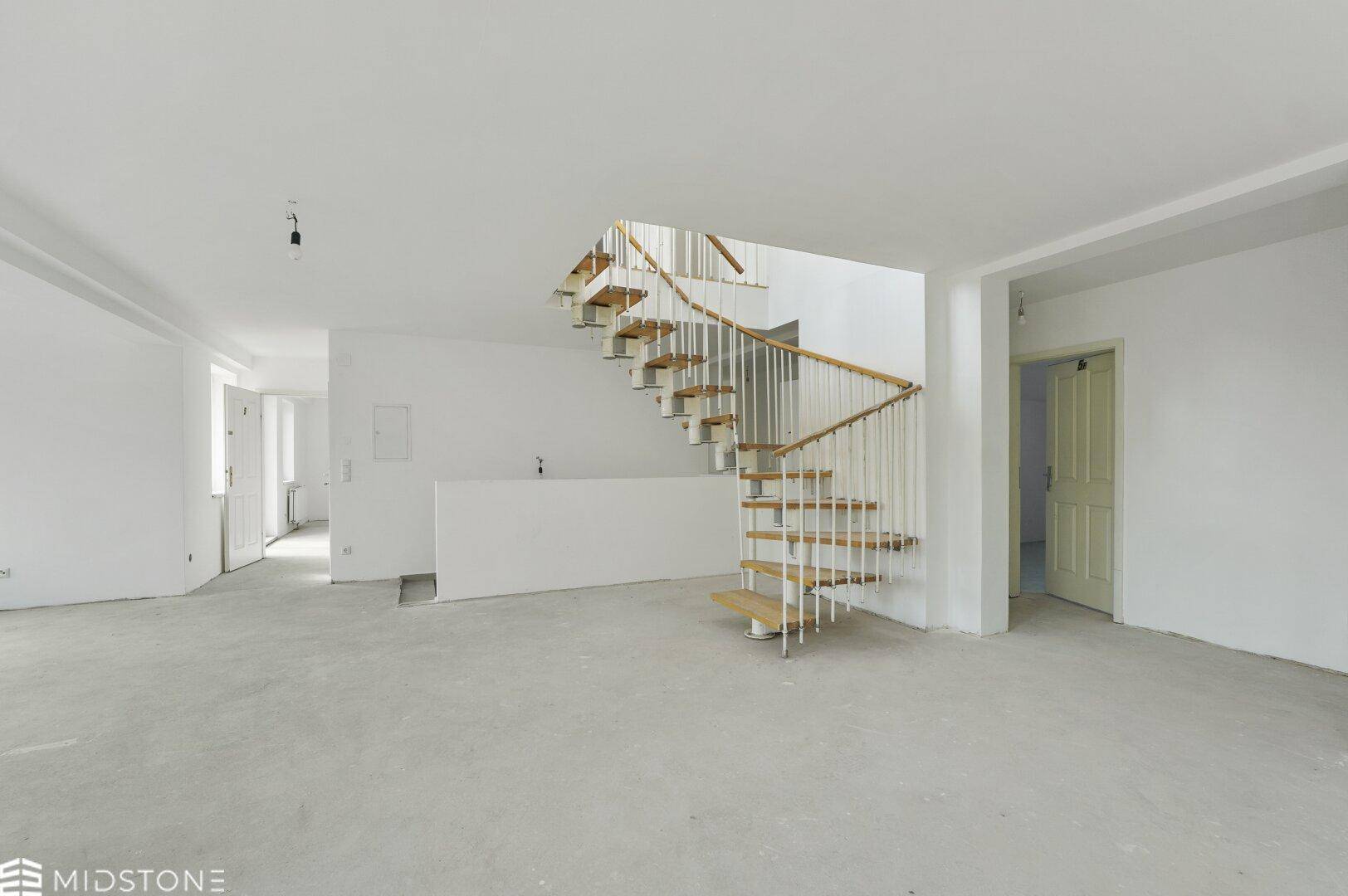 Großer, leerer offener Wohnbereich mit Wendeltreppe und Betonboden, bereit für die individuelle Einrichtung.