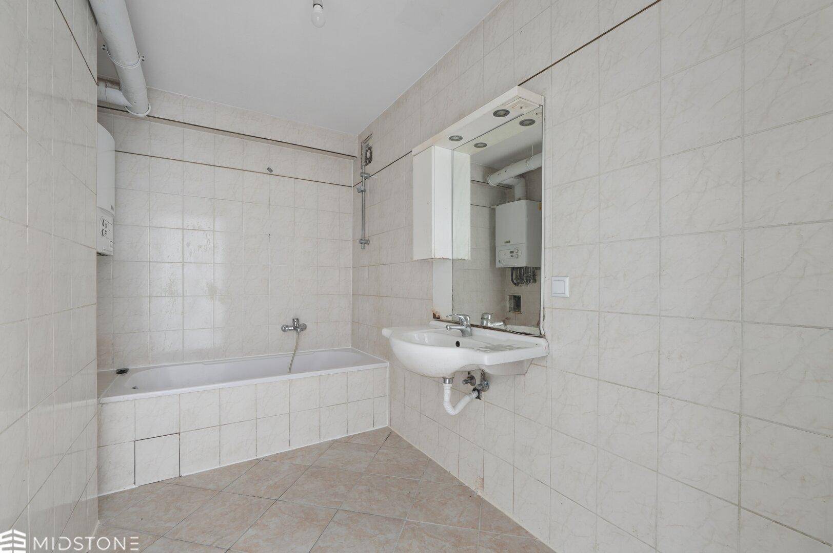 Älteres Badezimmer mit Badewanne, Waschbecken und beigefarbenen Fliesen, renovierungsbedürftig.