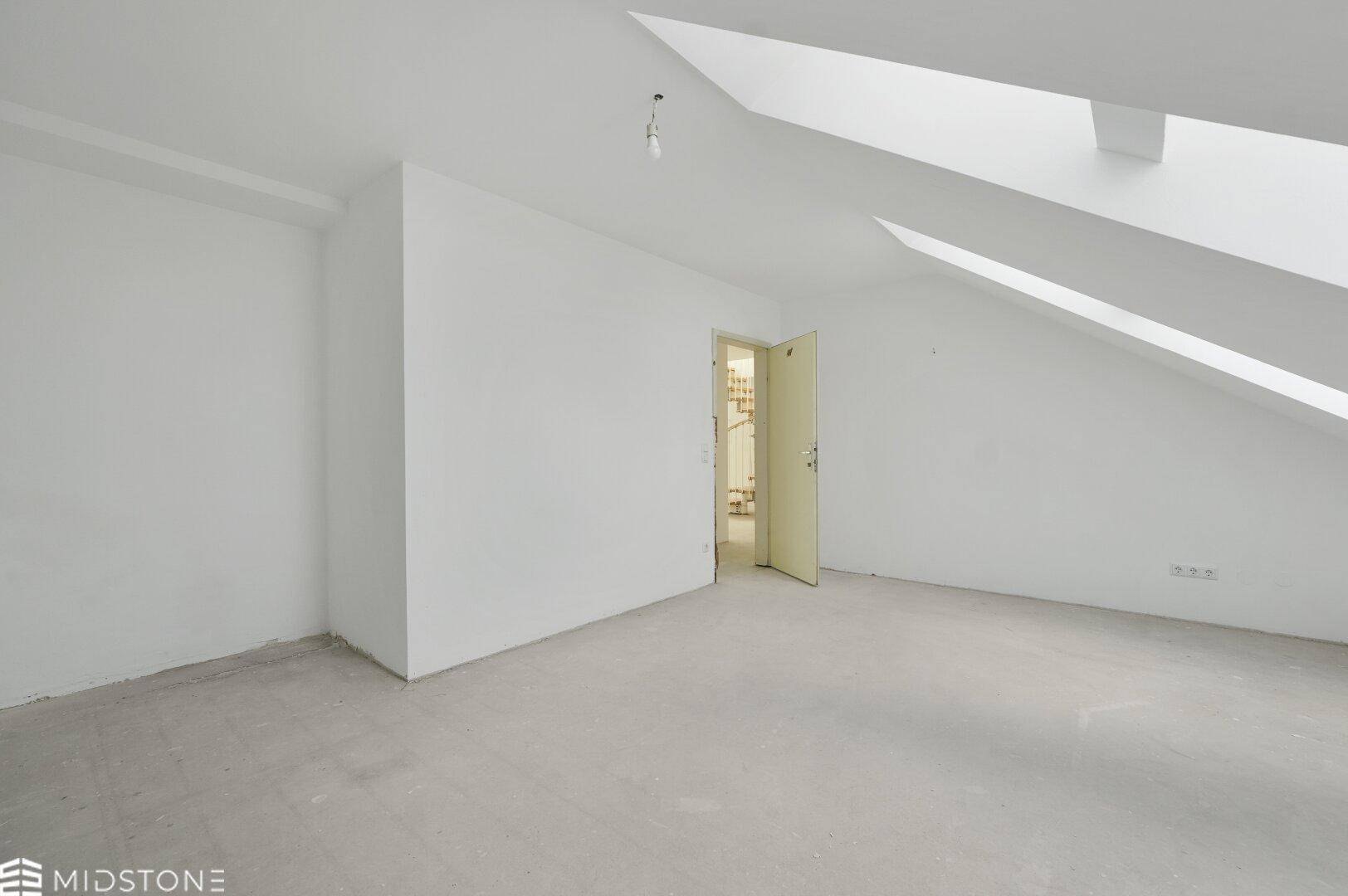 Leeres Dachgeschosszimmer mit schrägen Wänden und Betonboden, bereit für den Innenausbau.