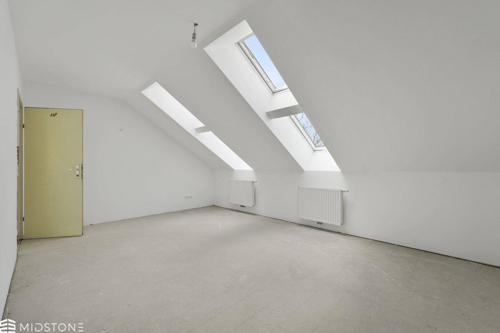 Helles Dachgeschosszimmer mit zwei Dachfenstern, schrägen Wänden und Betonboden.