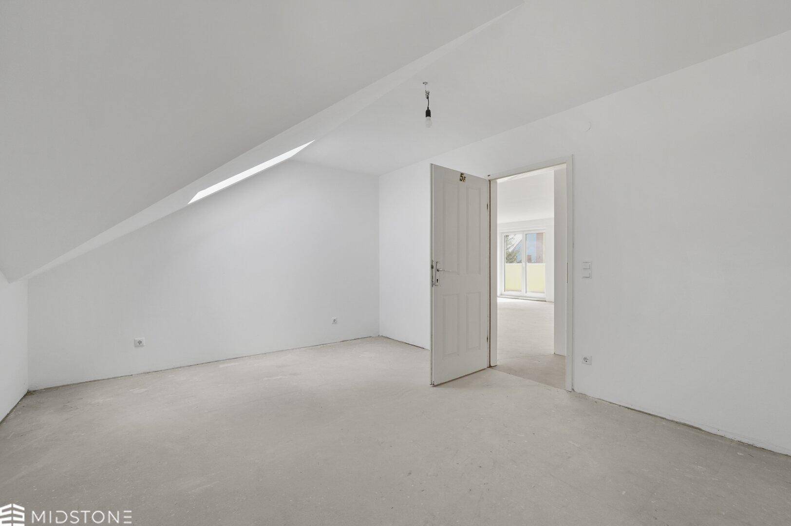 Leeres Dachgeschosszimmer mit schrägen Wänden und Betonboden, bietet viel Potenzial.