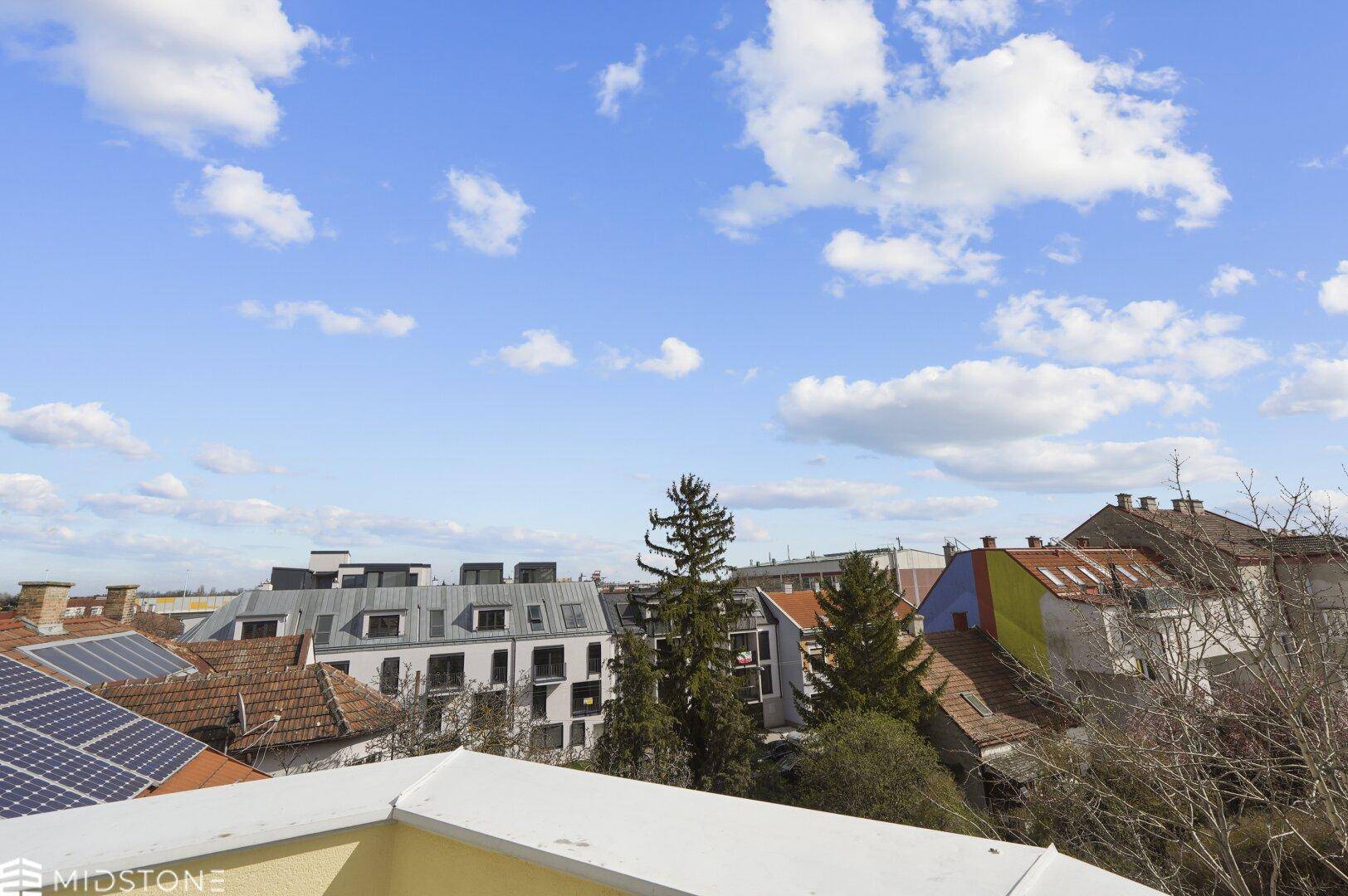 Weitblick über die Dächer der Nachbarschaft mit Bäumen und blauem Himmel.