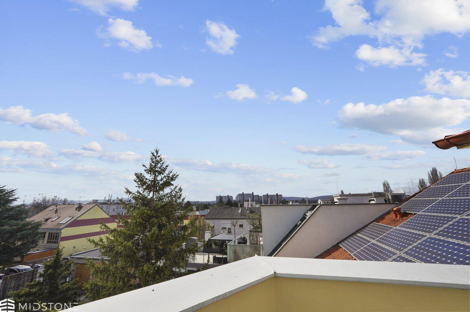 Ausblick über die Dächer der Stadt mit Bäumen und Solaranlagen auf den Häusern.