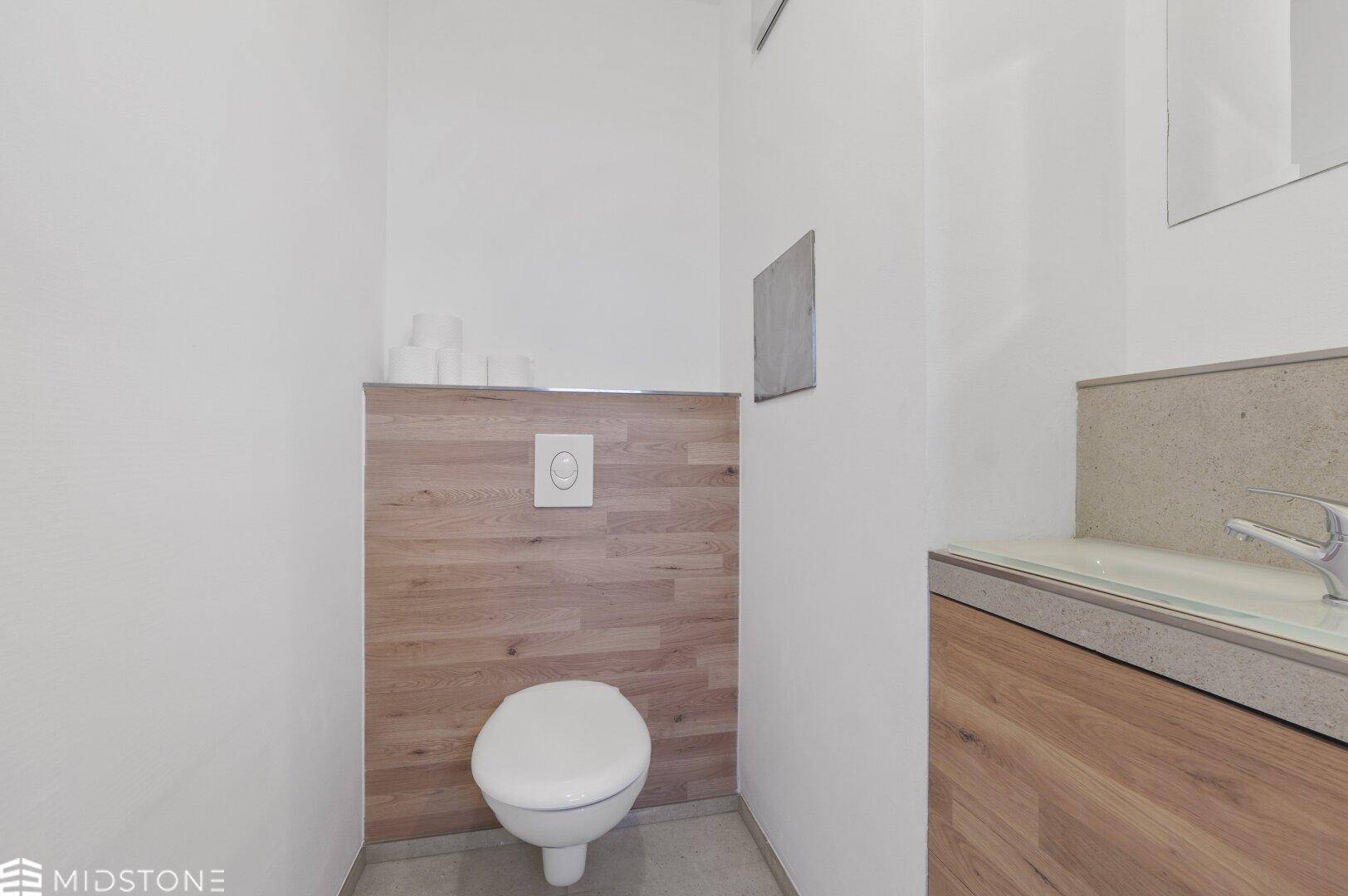 Modernes Gäste-WC mit wandhängender Toilette, Holzverkleidung und kleinem Waschbecken.