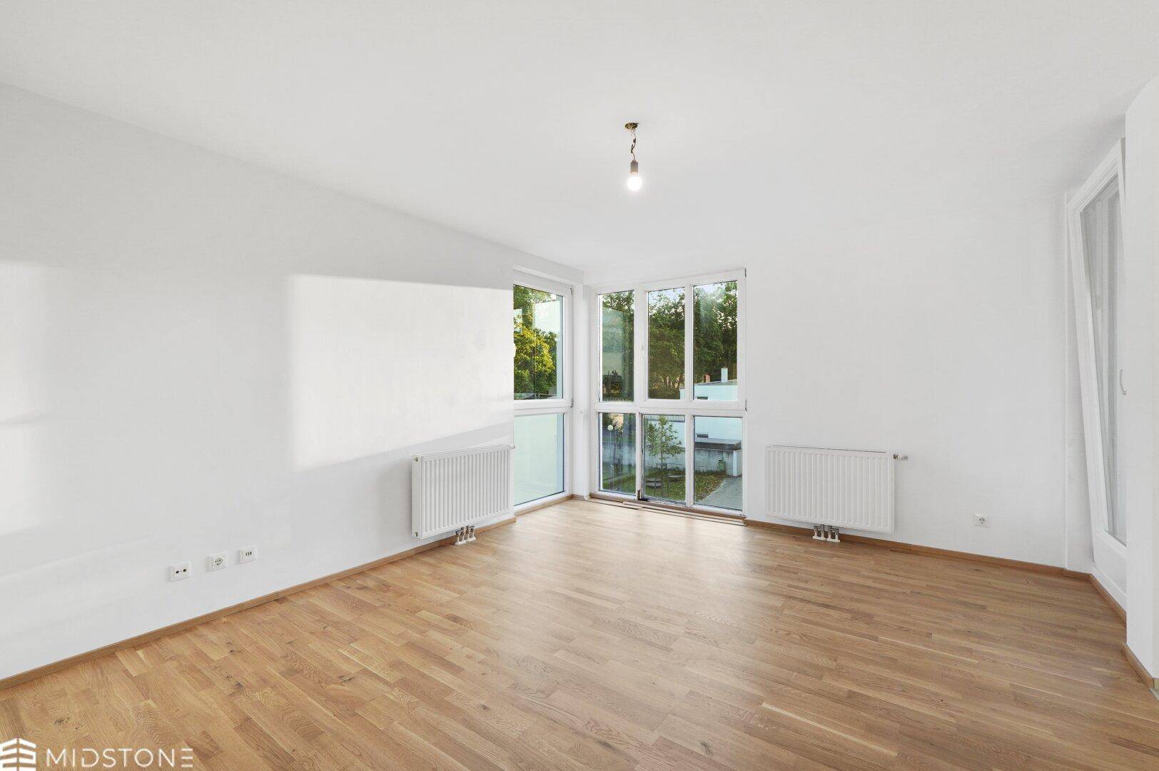 Helles Schlafzimmer mit Parkettboden und großen Fenstern, die viel Tageslicht hereinlassen.