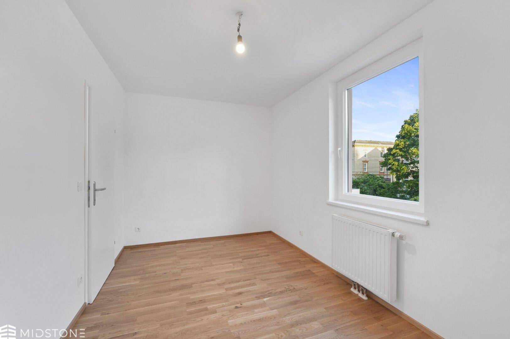 Geräumiges Schlafzimmer mit Parkettboden und einem Fenster, das viel Tageslicht bietet.