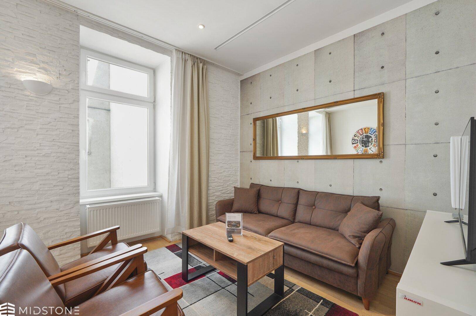 Gemütliches Wohnzimmer mit beigem Sofa, Ledersesseln und einem großen Spiegel an der Wand.