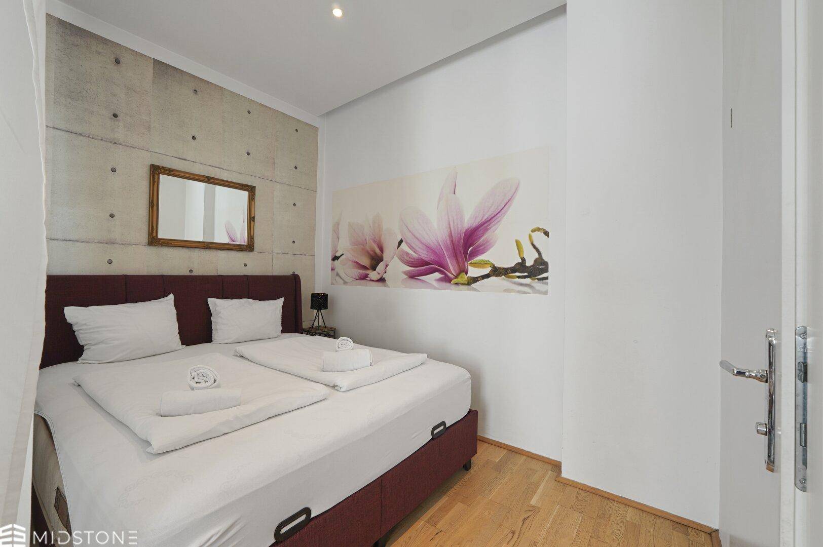 Schlafzimmer mit Doppelbett, Holzboden und einer modernen Wanddekoration über dem Bett.