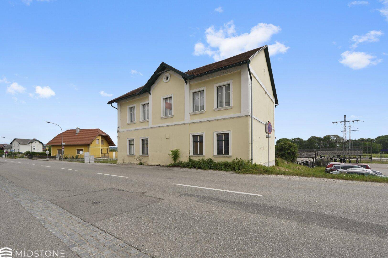 Weitwinkelansicht des gelben Gebäudes an der Straße, mit einem weiteren Haus in der Ferne und klarem Himmel.