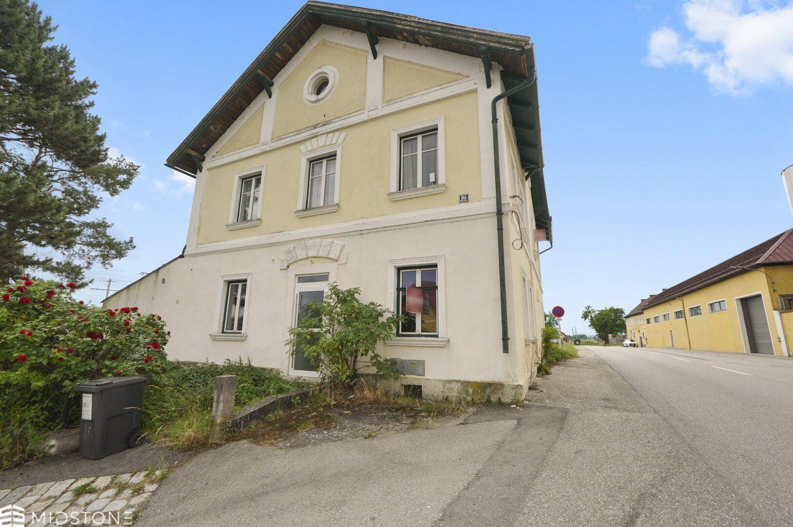 Ansicht des gelben Gebäudes von der Straße aus mit einem kleinen Vorgarten und blauem Himmel.