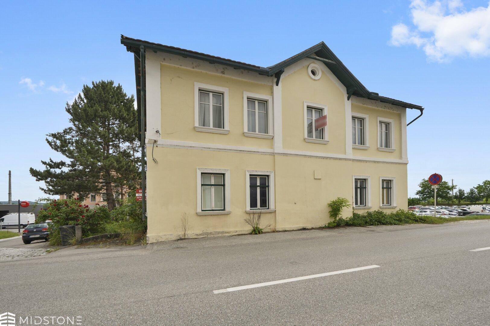 Seitenansicht des gelben Gebäudes mit Blick auf die Straße und einen entfernten Parkplatz unter blauem Himmel.