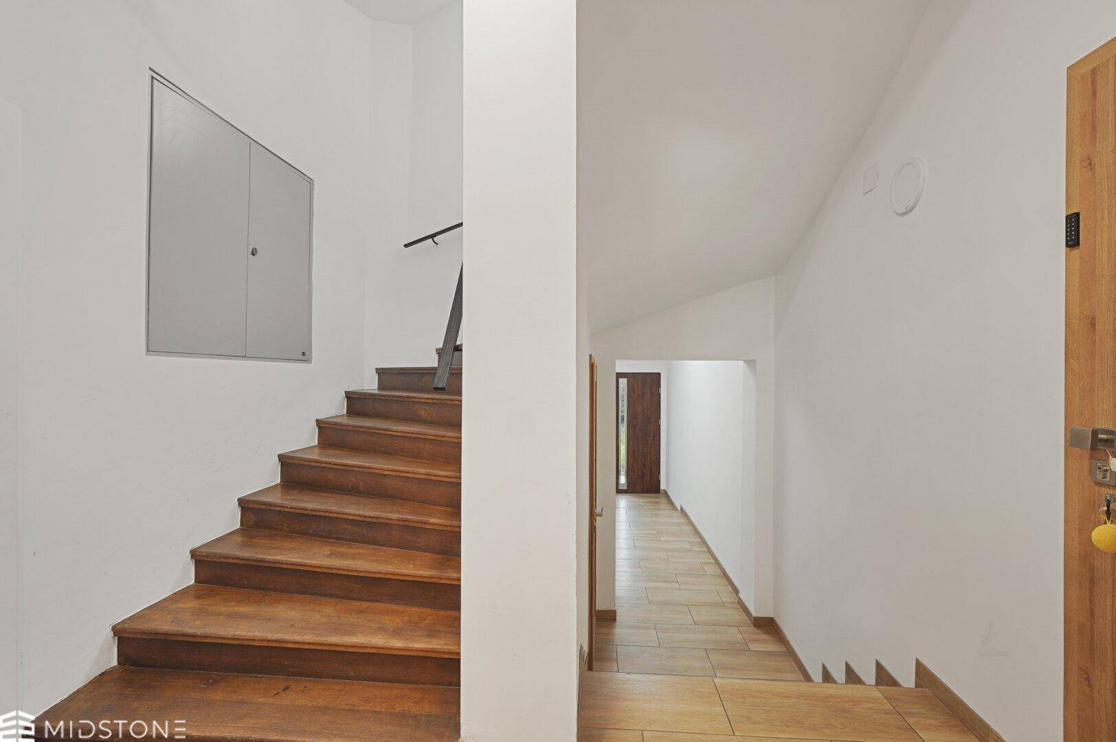 Treppenhaus mit Holzstufen und hellem Flur, der zu weiteren Räumen im Gebäude führt.