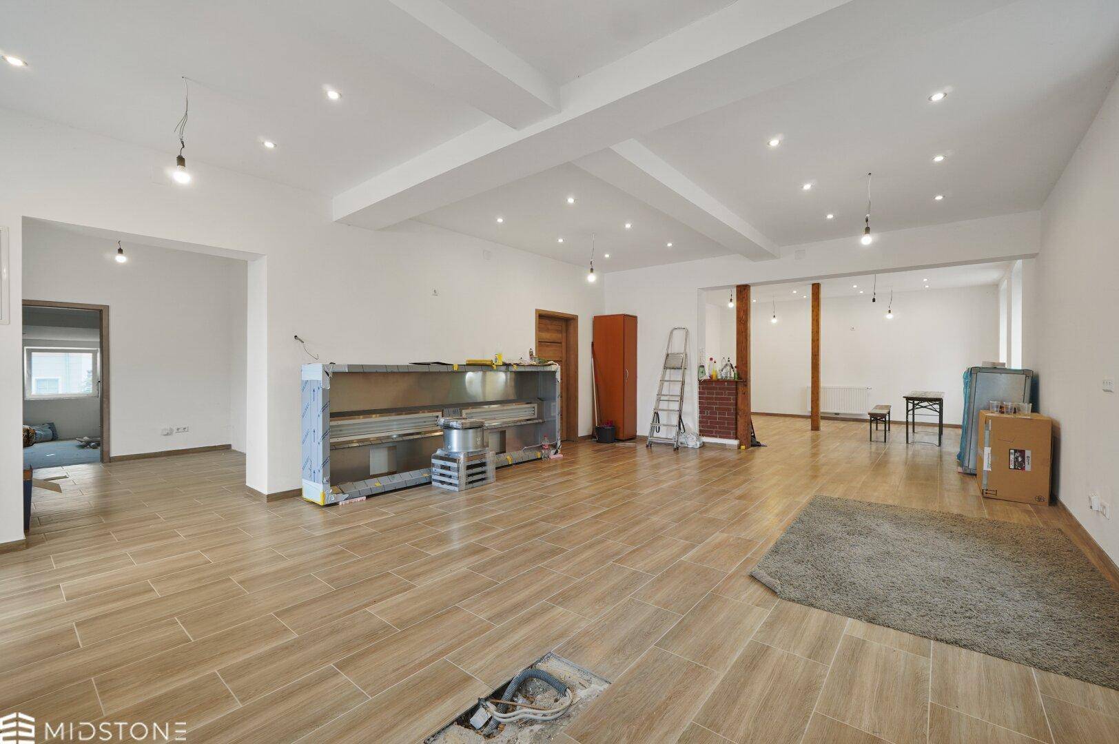 Großer, offener Raum mit Fliesenboden und sichtbaren Deckenbalken, derzeit im Umbau.