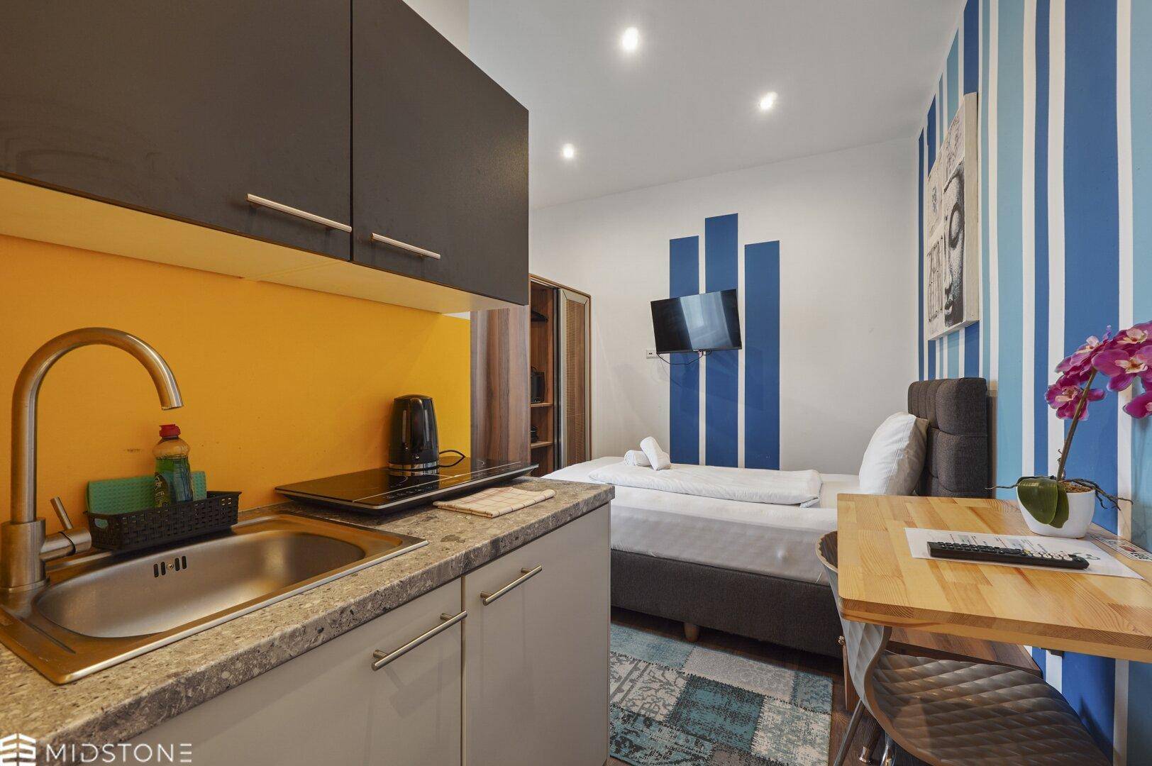 Studio-Apartment mit Küchenzeile, Schlafbereich und Buddha-Kunstwerk, farbenfroh und funktional.