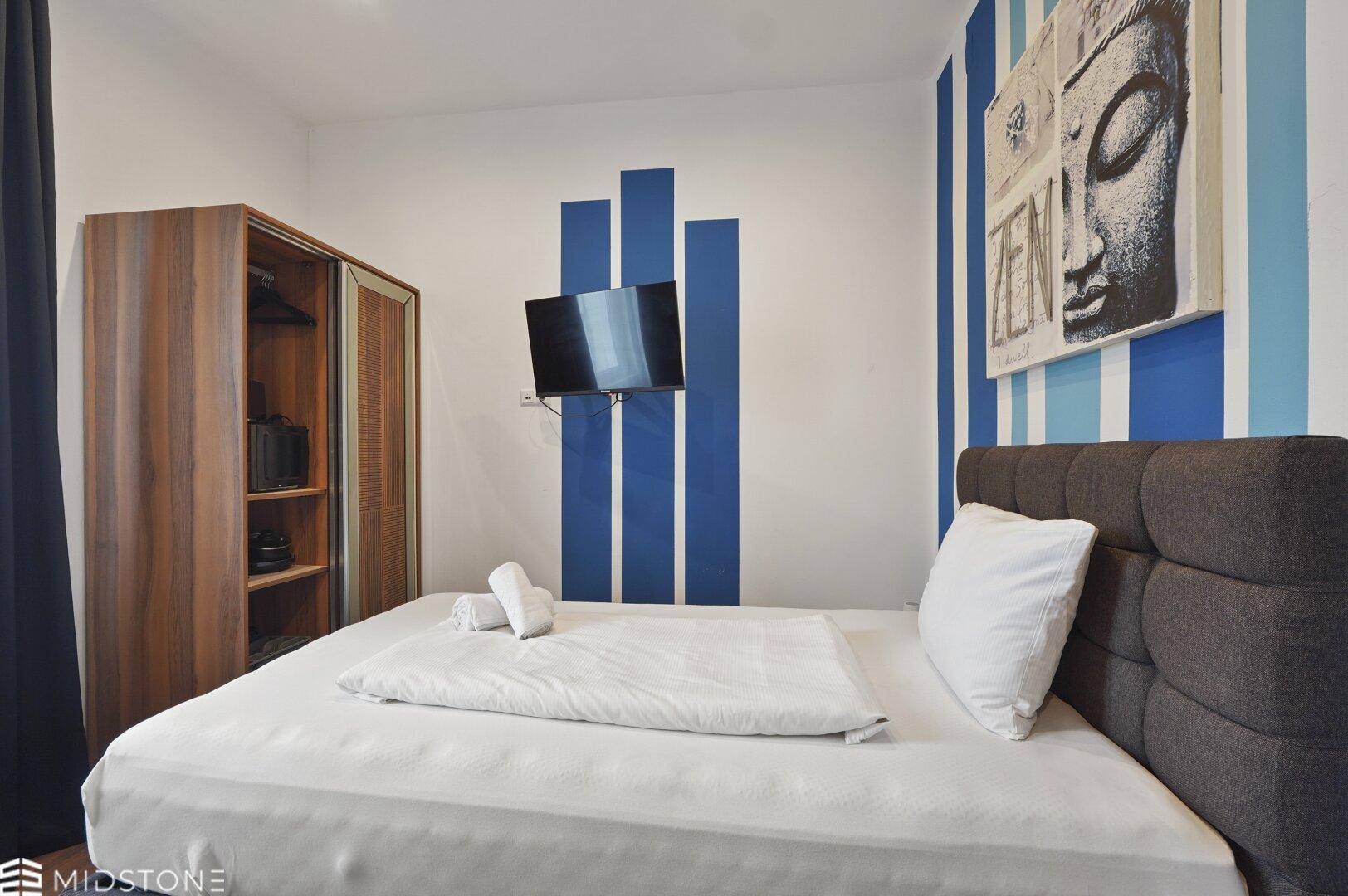 Schlafzimmer mit Doppelbett, Wandfernseher und blauen Streifen an der Wand, modern dekoriert.
