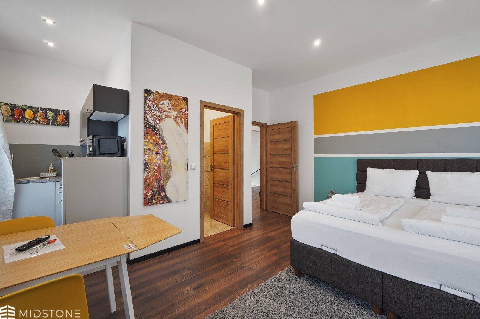 Studio-Apartment mit Küchenzeile, Schlafbereich und Kunstwerken an den Wänden, modern eingerichtet.