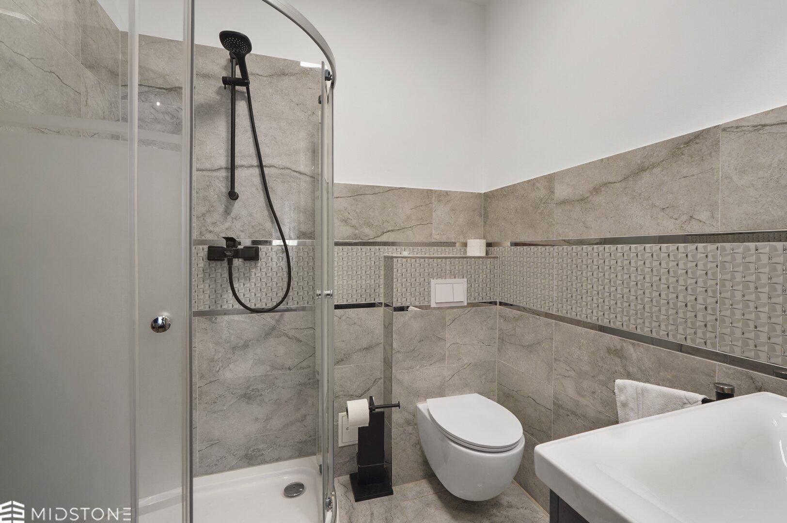 Modernes Badezimmer mit Duschkabine, grauen Fliesen und Wand-WC, funktional und hell.