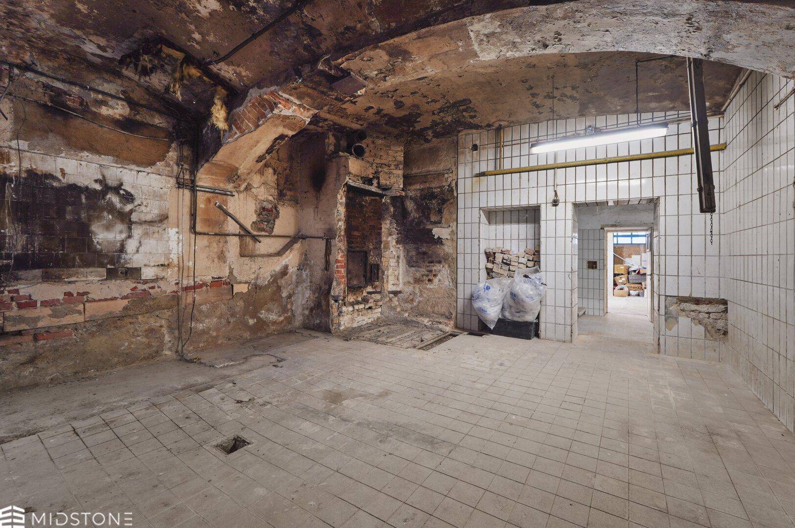 Rustikaler Kellerraum mit freiliegenden Ziegelwänden, Fliesenboden und sichtbaren Deckenstrukturen.
