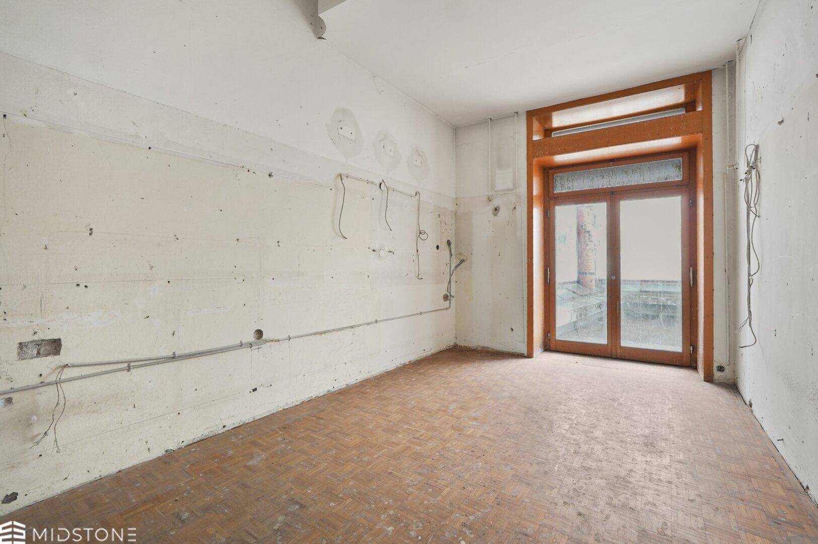 Heller, leerer Raum mit Holzboden und einer großen Holztür, die nach draußen führt.