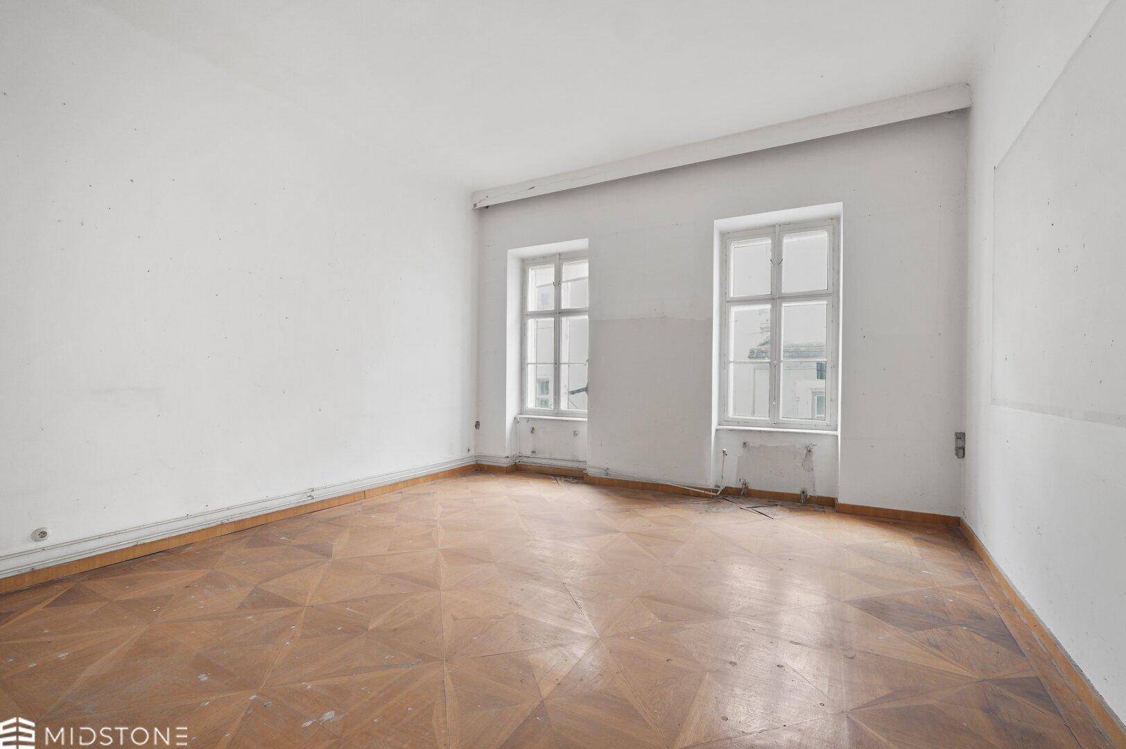 Heller, leerer Raum mit Parkettboden und zwei großen Fenstern, ideal für Wohnzwecke.