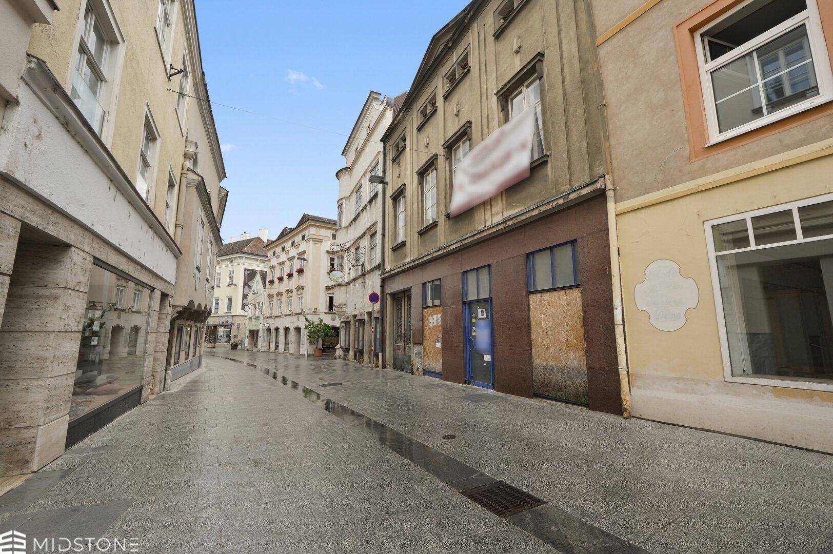 Historische Straße mit alten Gebäuden und gepflastertem Gehweg in einer malerischen Stadtansicht.