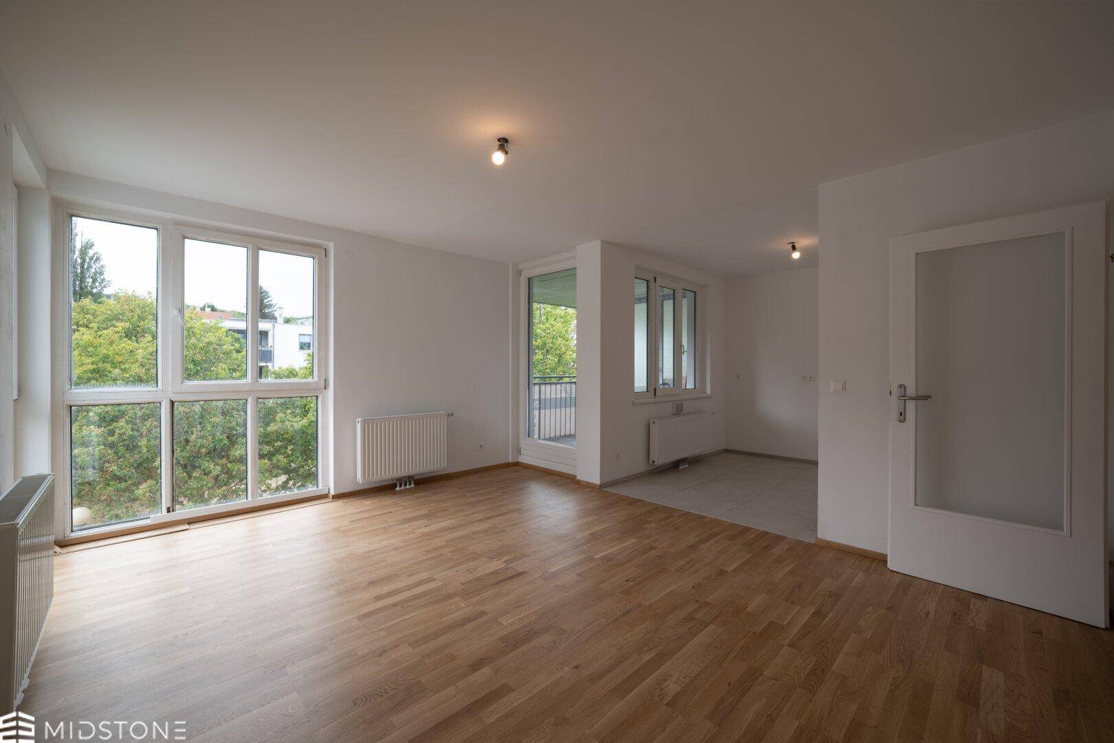 Geräumiges Wohnzimmer mit großen Fenstern, Parkettboden und viel Tageslicht.