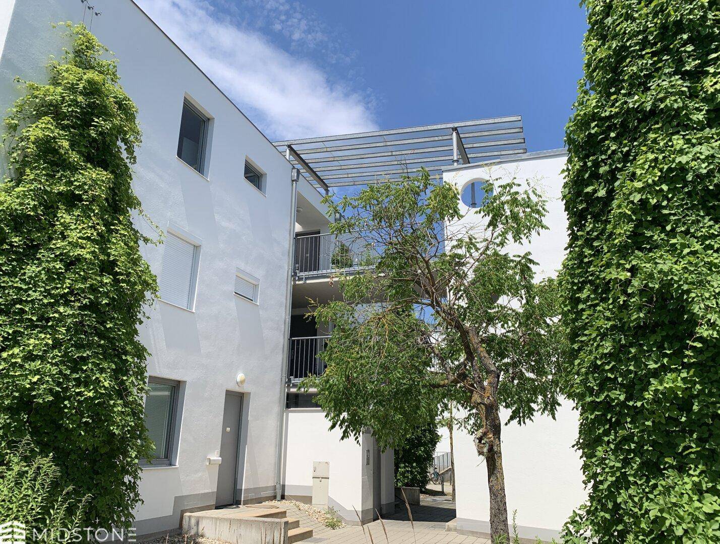 Moderne Wohnanlage mit weißer Fassade, begrünten Wänden und Zugang zu den oberen Etagen.