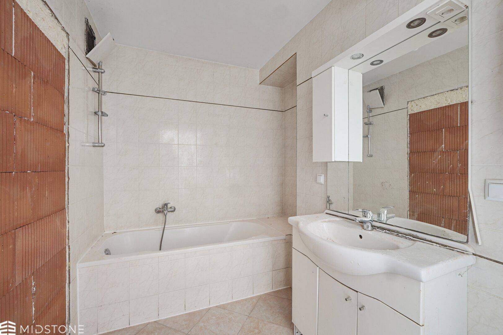 Badezimmer in Renovierungszustand mit Badewanne, Waschbecken und Fliesen.