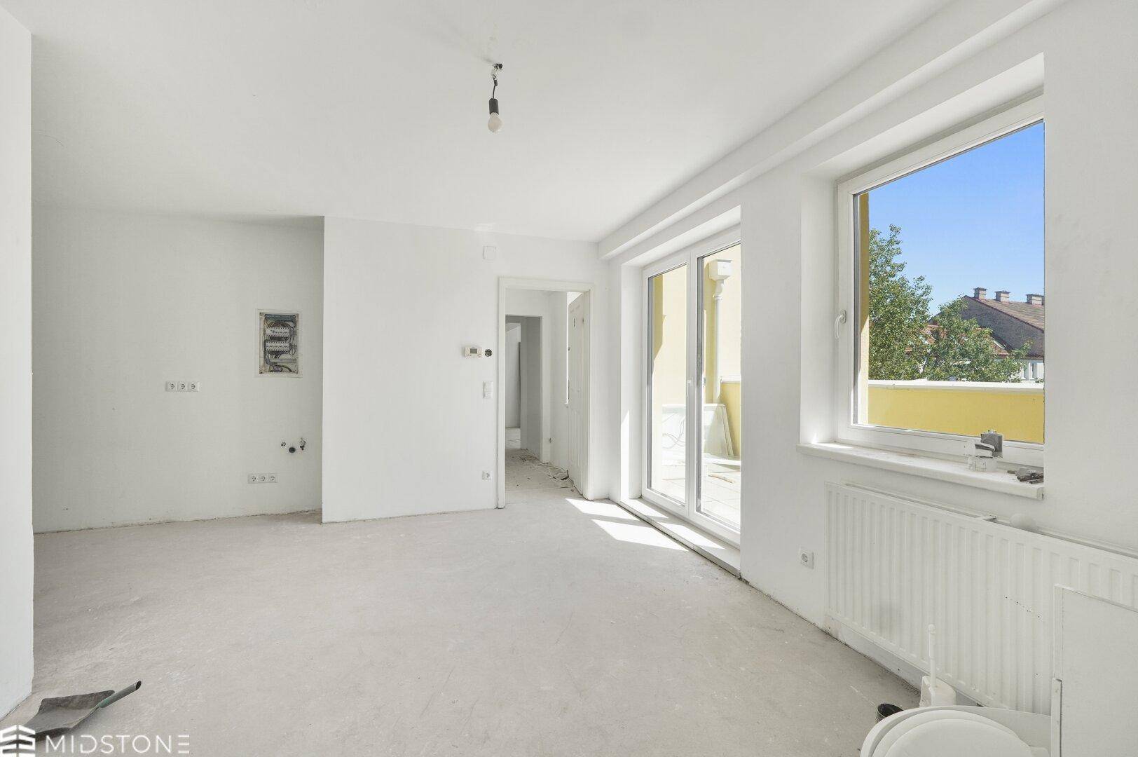 Heller, unmöblierter Wohnbereich mit großen Fenstern und Zugang zur Terrasse.