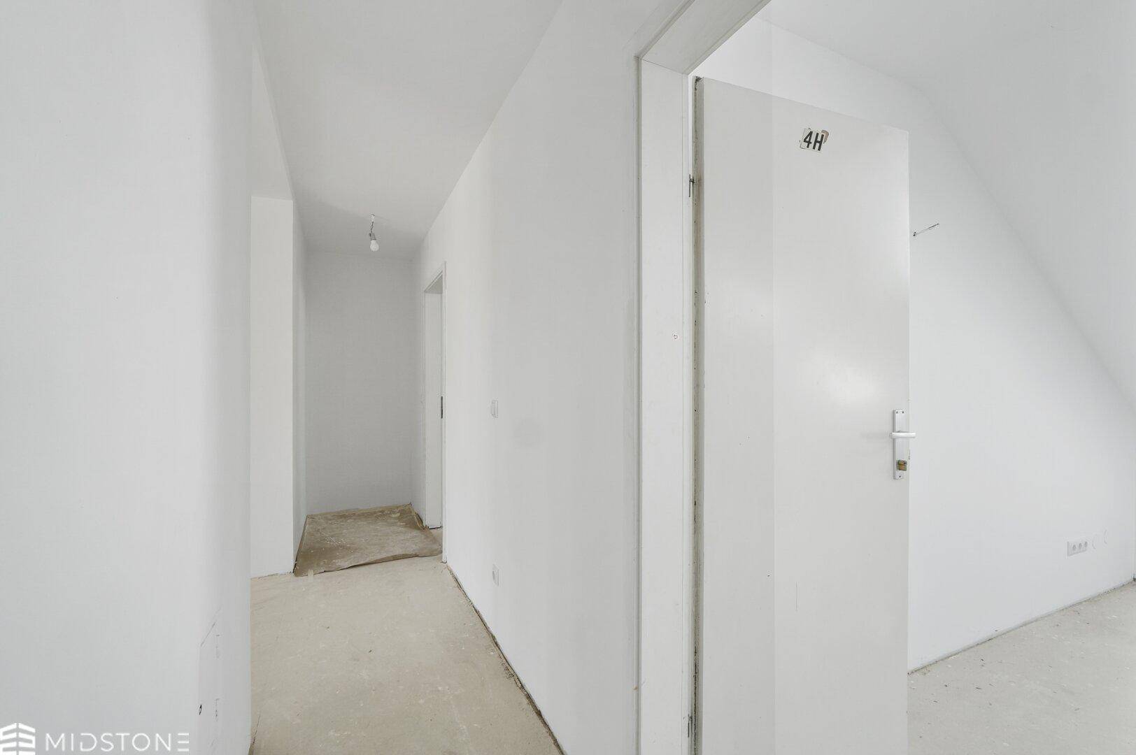 Leerer Flur im Rohbau mit weißen Wänden und einer Tür, bereit für den Ausbau.