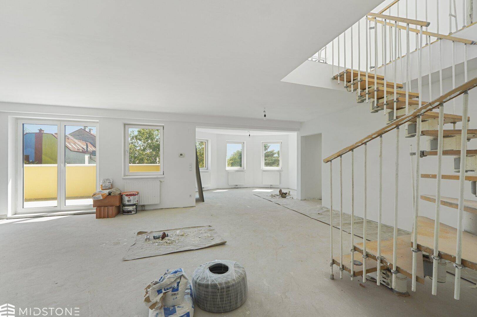 Heller, offener Wohnbereich im Rohbau mit Wendeltreppe und Zugang zu einem Balkon.
