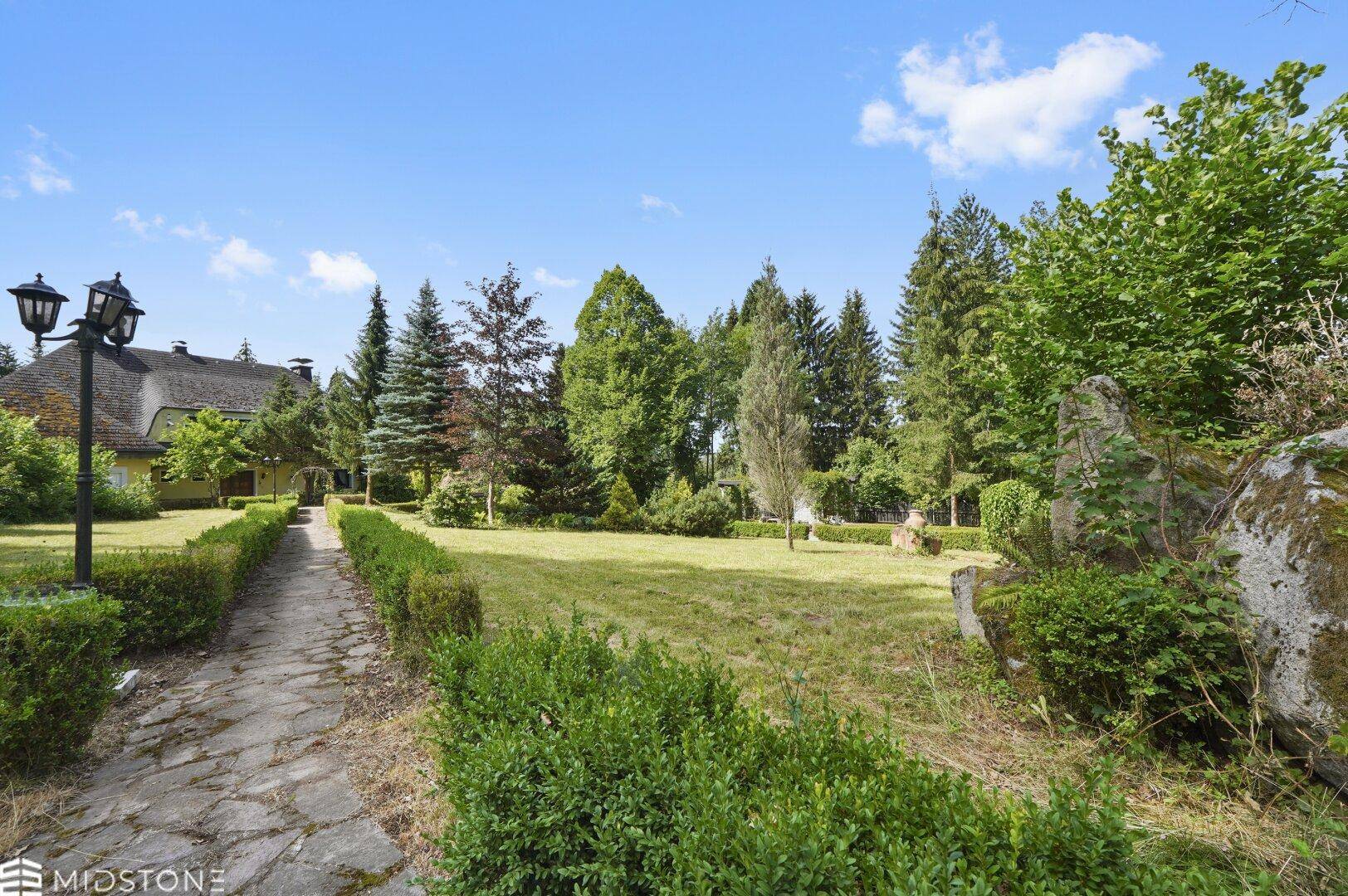 Weitläufige Rasenfläche mit Bäumen, Steinweg und Laterne, Teil des großen Gartens.