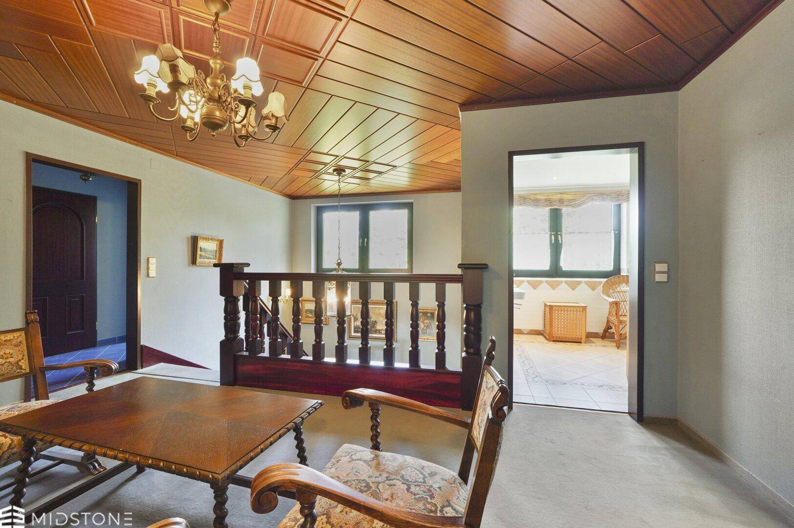 Obergeschoss-Flur mit Holzdecke, Kronleuchter und Blick in ein angrenzendes Zimmer.