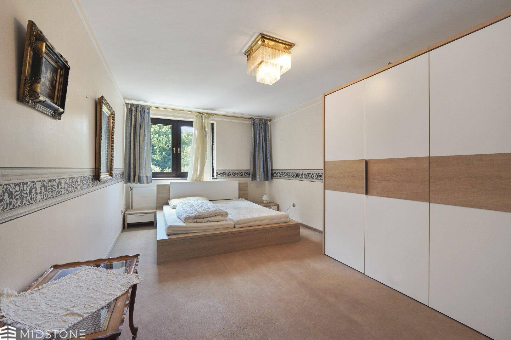Schlafzimmer mit Doppelbett, modernem Kleiderschrank und Fenster mit Blick ins Grüne.