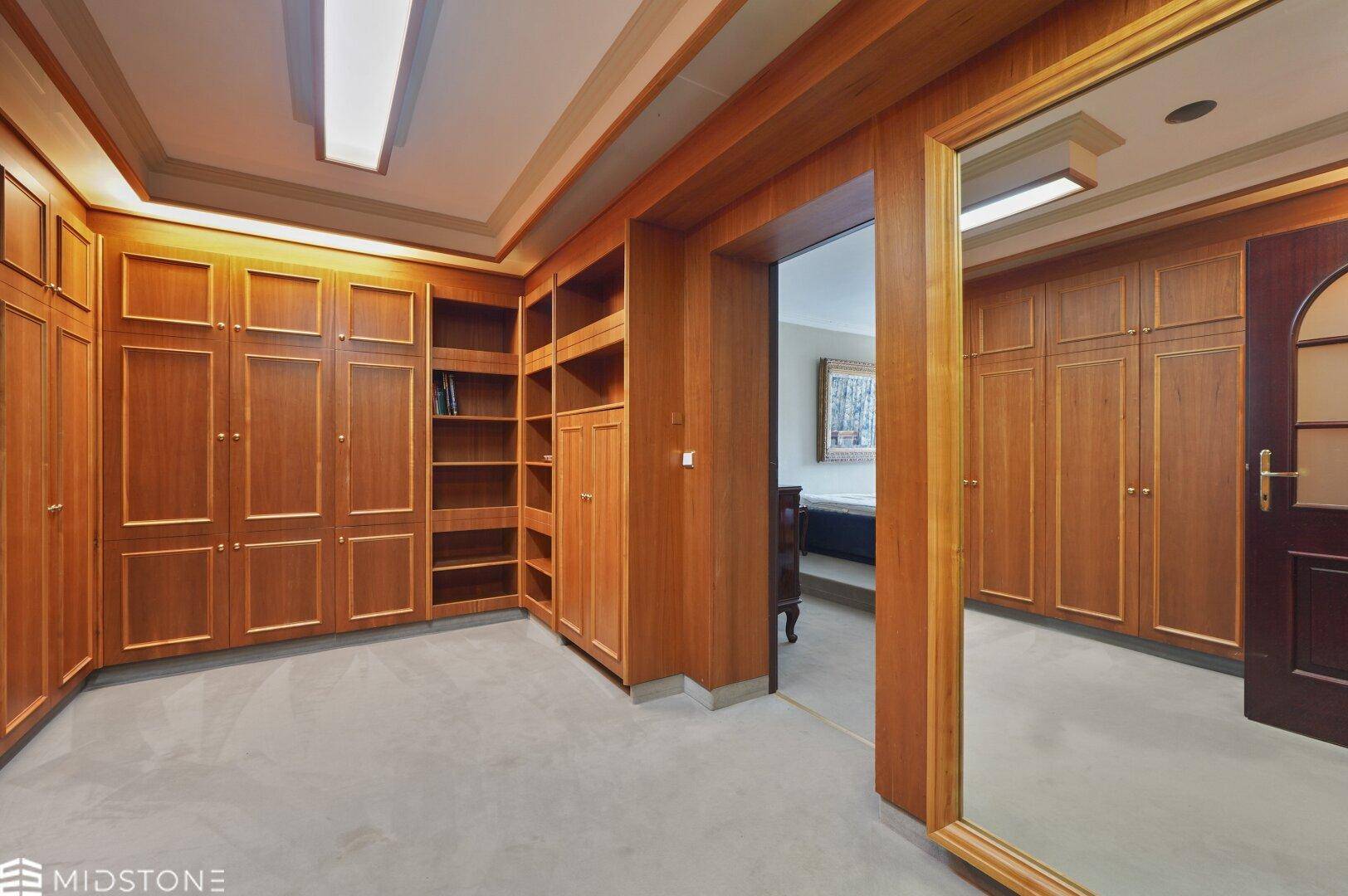 Geräumiger begehbarer Kleiderschrank mit maßgefertigten Holzschränken und Regalen.