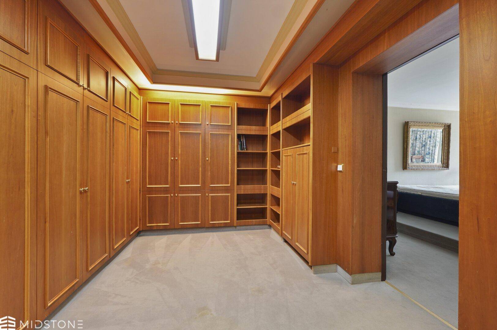 Begehbarer Kleiderschrank mit Holzschränken und Zugang zu einem angrenzenden Schlafzimmer.