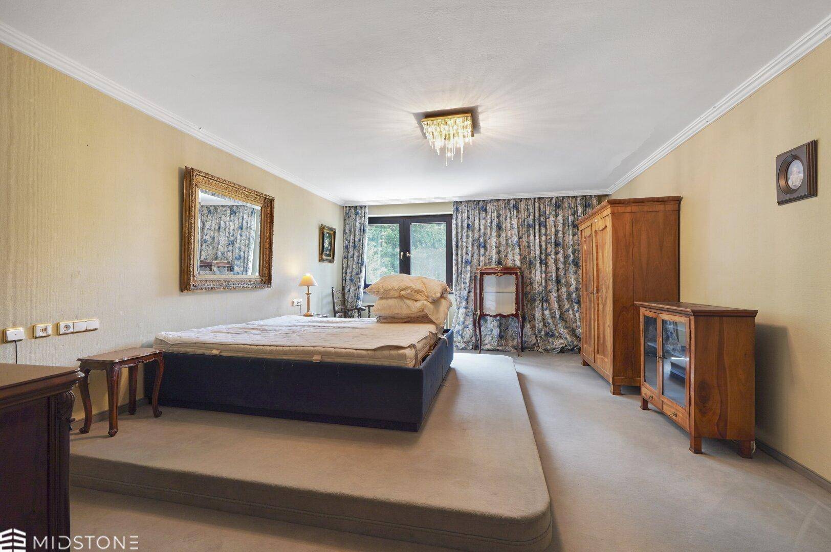 Großes Schlafzimmer mit erhöhtem Bett, traditionellen Holzmöbeln und Zugang zum Balkon.