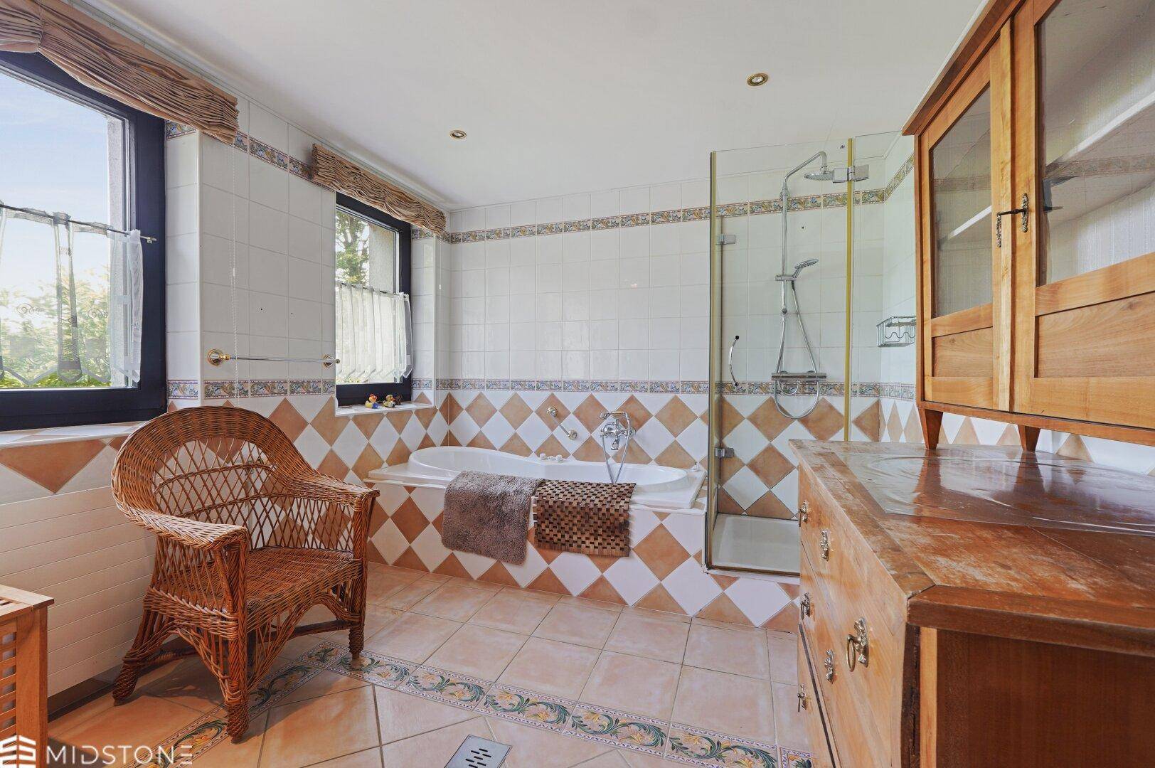 Badezimmer mit Badewanne, Duschkabine, gemusterten Fliesen und einem Holzschrank.