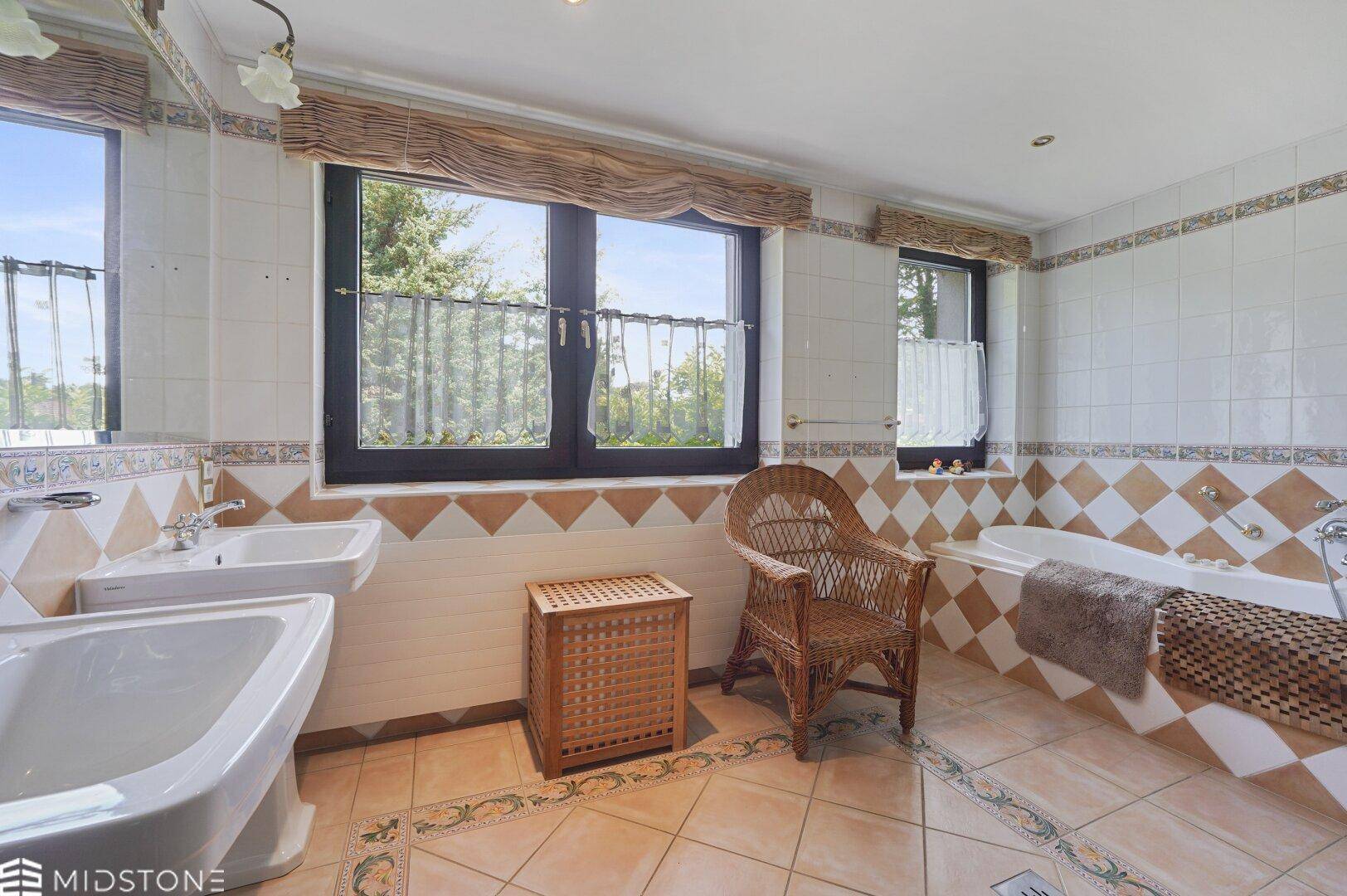 Badezimmer mit gemusterten Fliesen, Badewanne, Einzelwaschbecken und einem Fenster mit Blick ins Grüne.